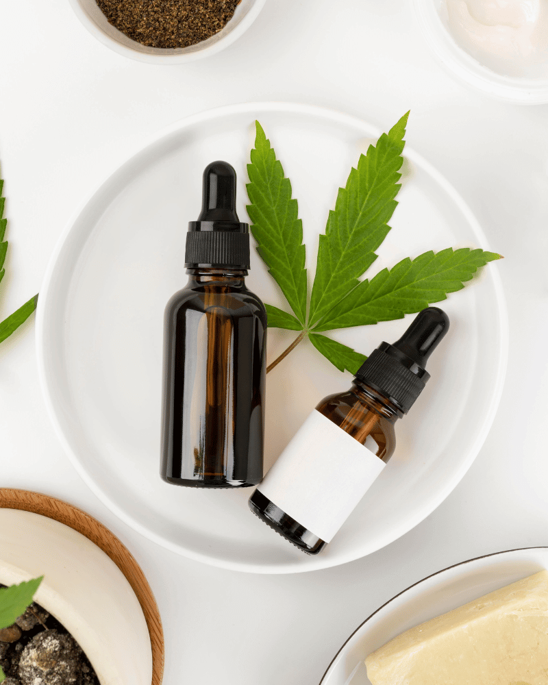 Sticluță de ulei CBD pe o farfurie albă cu frunză de cânepă