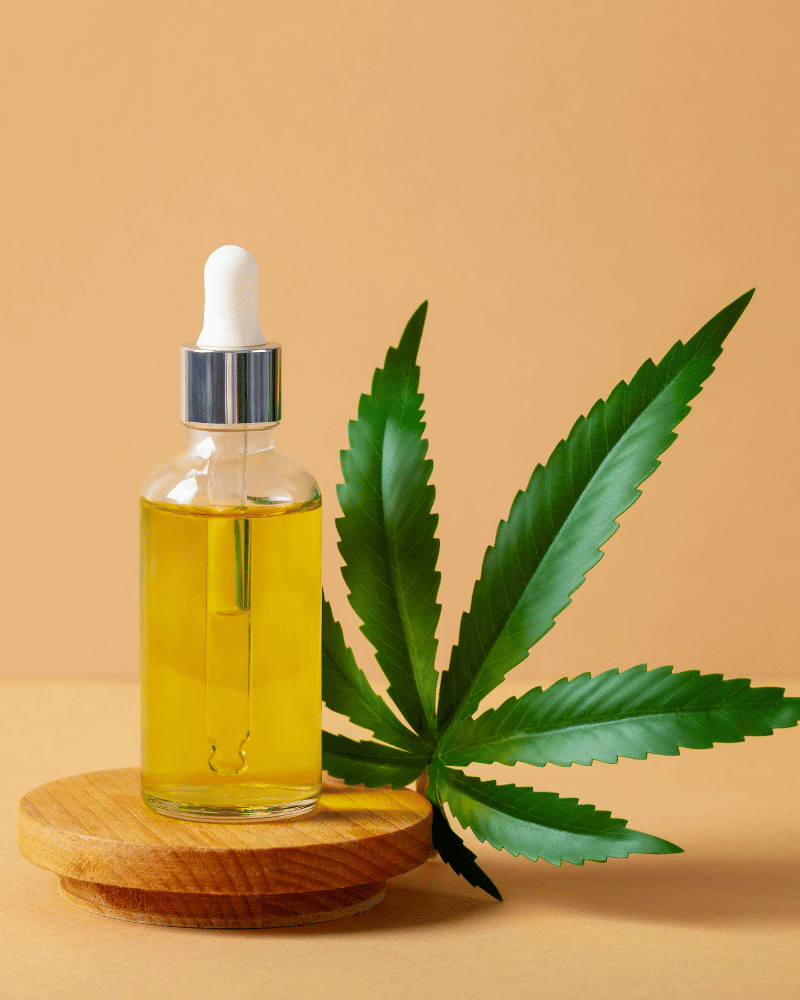 Ulei CBD pe o tavă de lemn cu o frunză de canabis în fundal